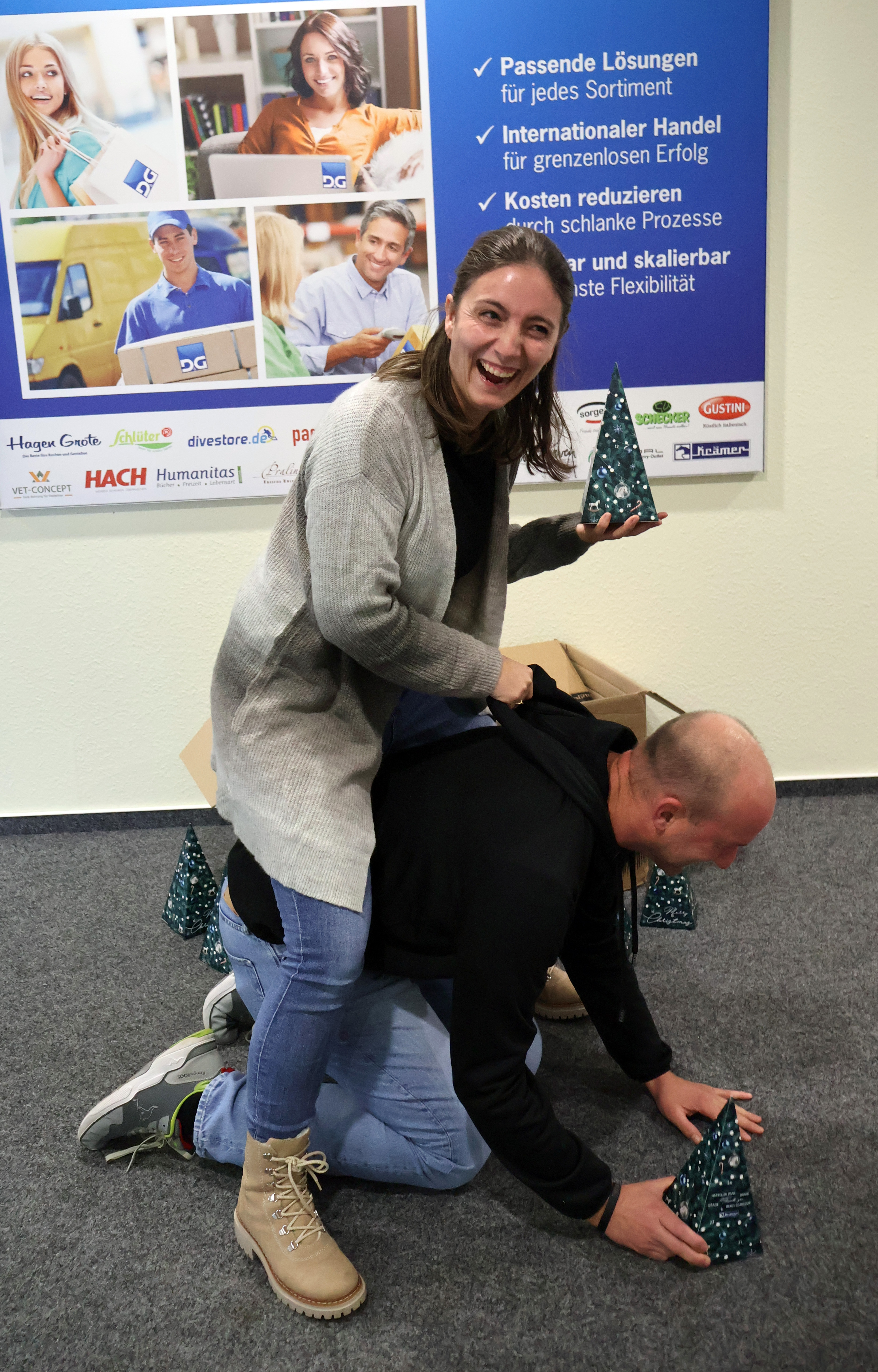 Mitarbeiterin macht Quatsch mit Mitarbeiter und sitzt auf seinem R&uuml;cken wie bei einem Pferd